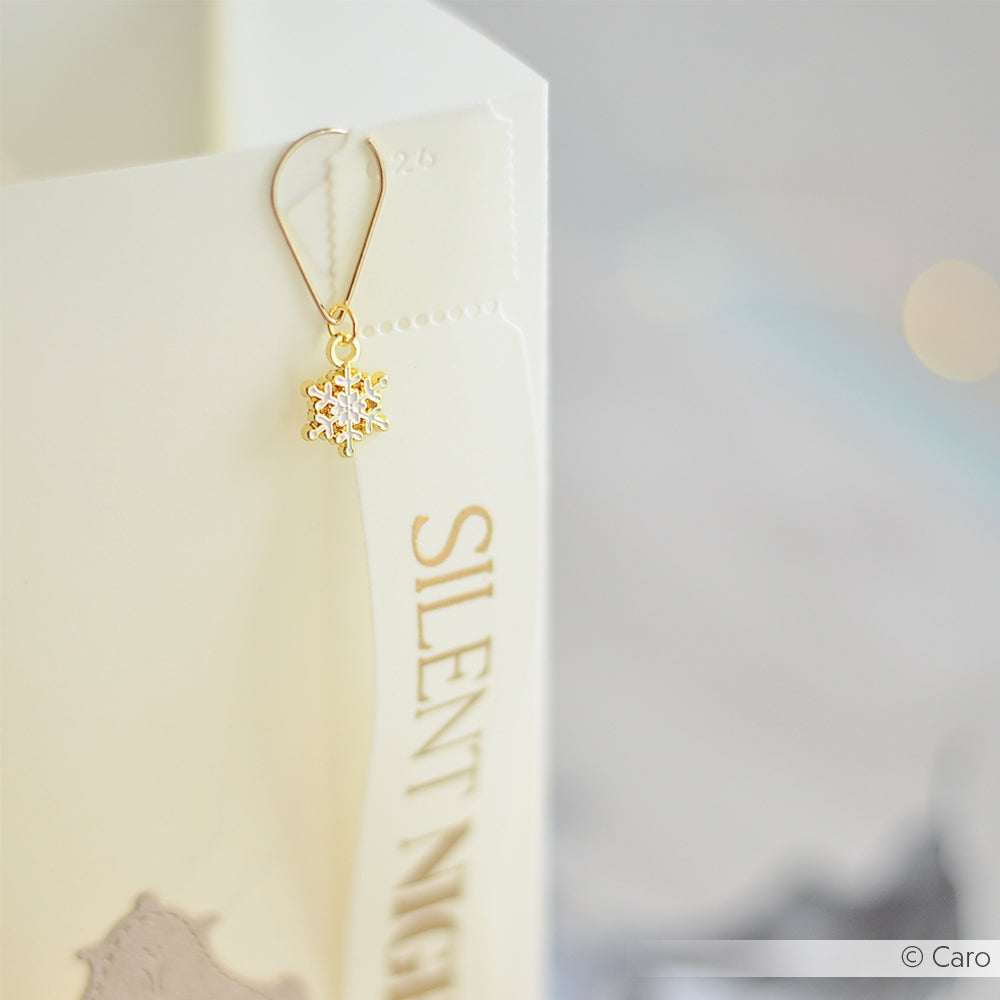 Goldener Schneeflocken-Ohrring von Alexandra Renke, inspiriert von Charm Eiskristall, mit einem Edelstein und einer weißen Stille-Nacht-Papiertüte.