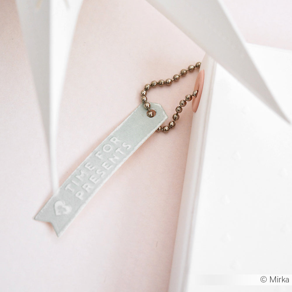 Ein Metallanhänger an einer Kugelkette trägt die Aufschrift TIME FOR PRESENTS vor einem zartrosa und weißen Hintergrund und sorgt für festliche Stimmung bei Ihren Projekten mit Alexandra Renke Stanzsystemen oder Cut & Emboss Folder.