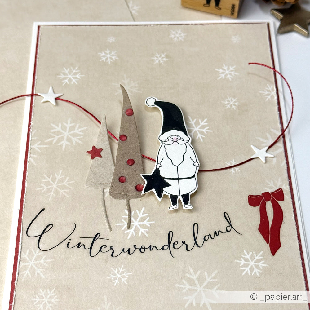 Handgefertigte Winterkarte von Alexandra Renke mit einem Weihnachtsmannausschnitt, Bäumen, Sternen, dem Text "Winterwonderland" auf einem Schneeflockenhintergrund und dem Rub-On Festlichkeiten Winterwald für einzigartige Winterwaldmotive.