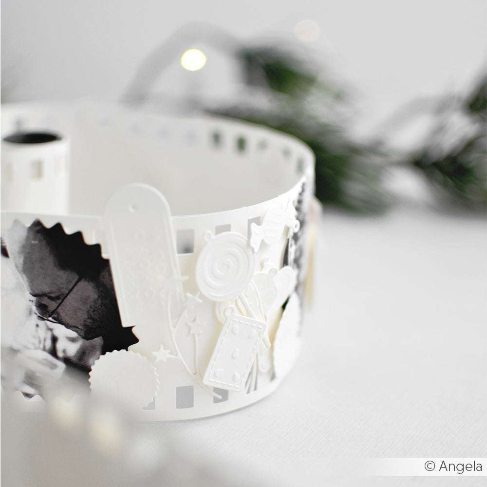 Eine Nahaufnahme eines weißen dekorativen Papierstreifens, der mit dem Alexandra Renke Cut & Emboss Folder hergestellt wurde, mit weihnachtlichen Motiven und verschwommenem Grün im Hintergrund.