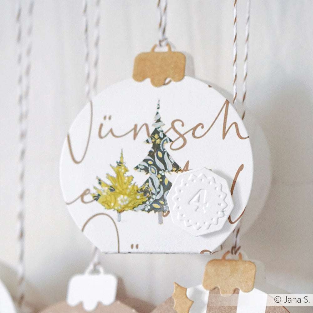 Rundes Ornament von Alexandra Renke mit zwei Weihnachtsbäumen, einer Schneeflocke und der Zahl 4, hergestellt mit Zahlen Etiketten und Cut & Emboss Folder, an einer Schnur hängend.