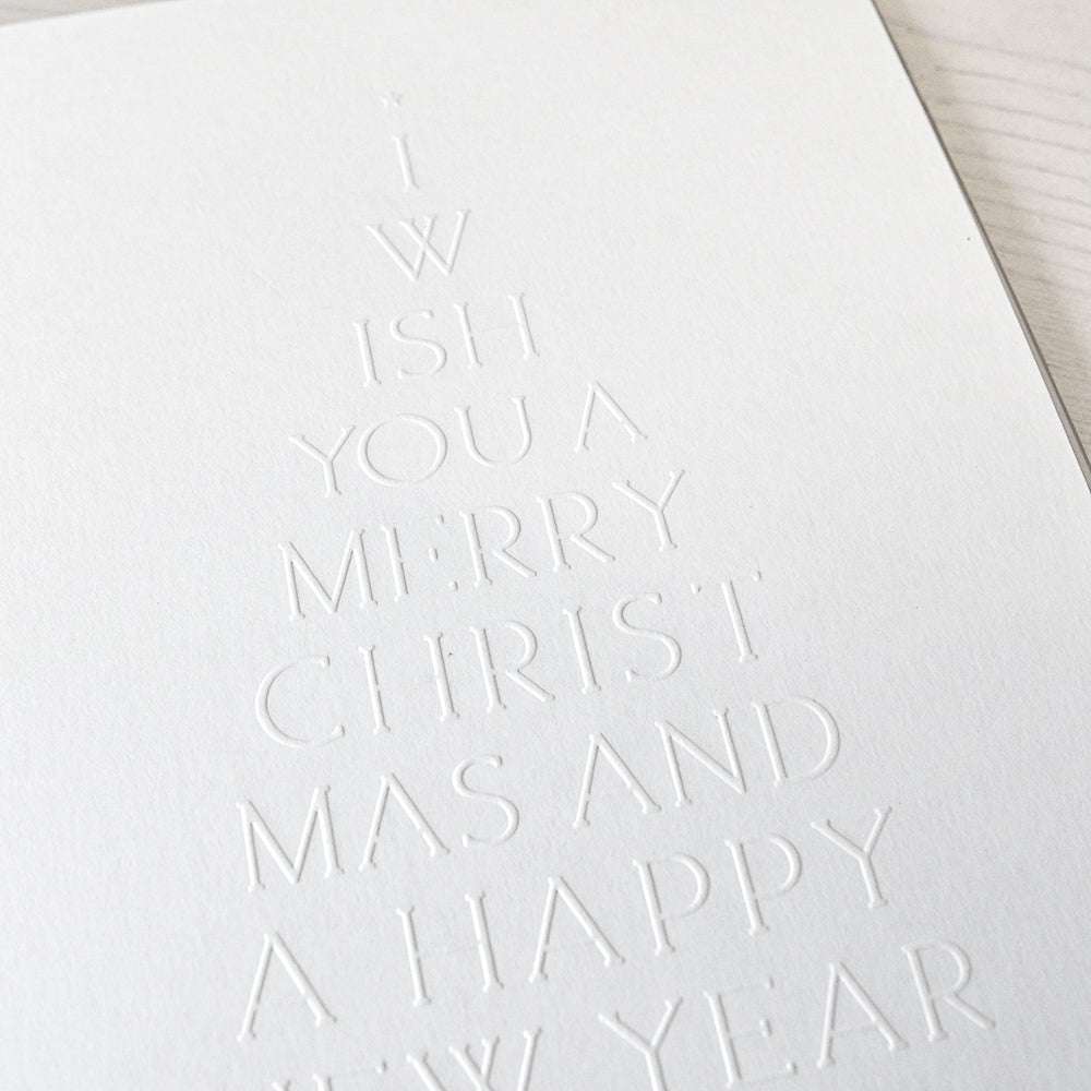 Weiße Karte mit dem Prägefolder von Alexandra Renke und dem geprägten Text "Typo Tanne Merry Christmas" in Form eines festlichen Baumes.
