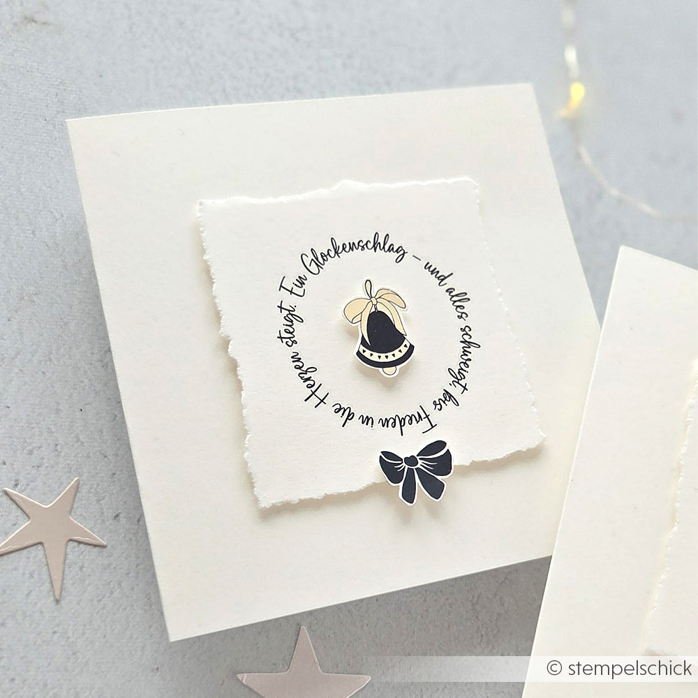 Eine handgefertigte Karte von Alexandra Renke mit einer Glocke und einer Schleife, einem kreisförmigen deutschen Text auf strukturiertem weißem Papier - ideal für Bastelprojekte oder in Kombination mit Rub-On Festlichkeiten für zusätzliches festliches Flair.