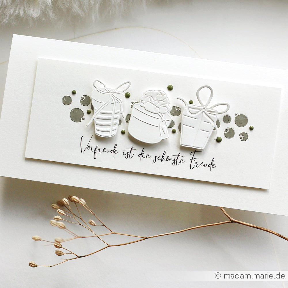 Weiße Karte von Alexandra Renke mit drei geprägten Geschenkboxen, deutschem Text und grünen Punkten; getrocknete Blumen auf der Vorderseite - ideal für Rub-On Festlichkeiten oder Adventslicht-Feiern.