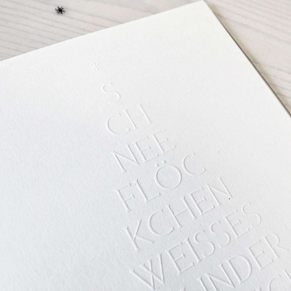 Weißer geprägter Text auf weißem Papier bildet mit dem Alexandra Renke Prägefolder ein minimalistisches Weihnachtsbaumdesign in dreieckiger Form.