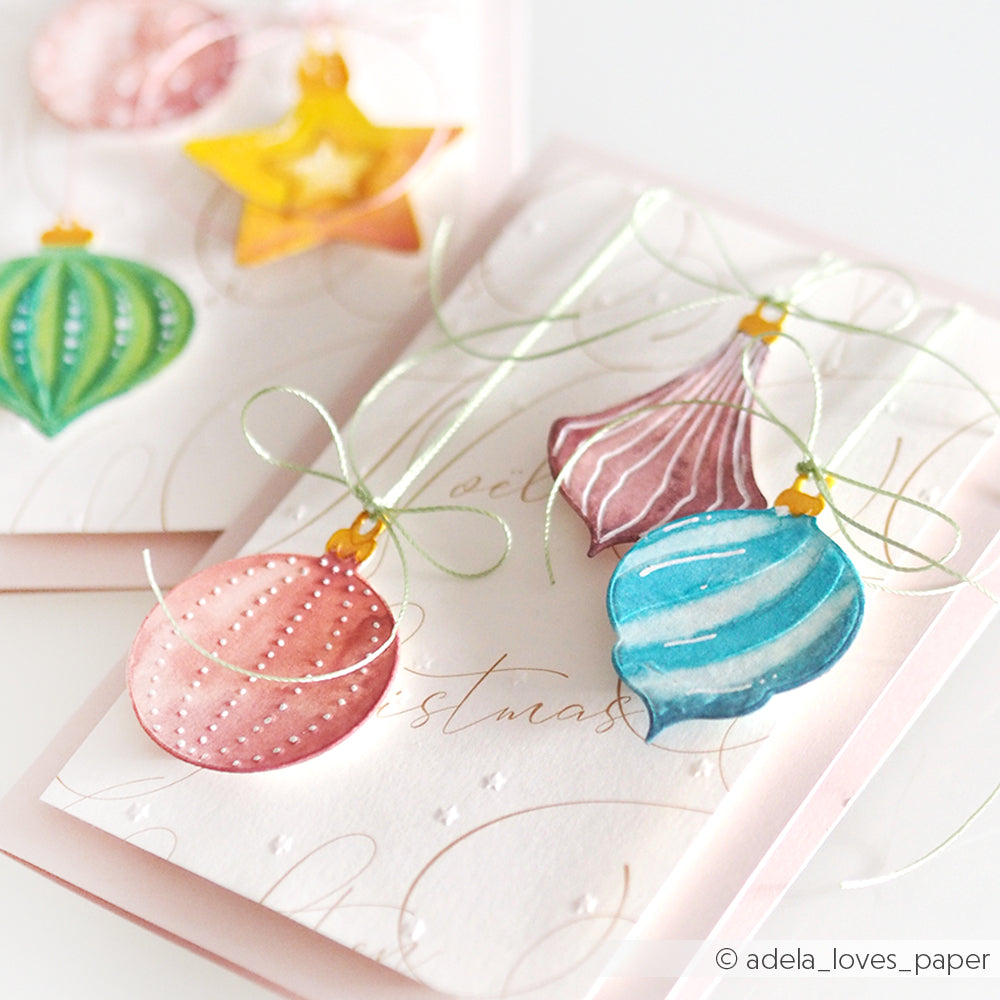 Eine handgefertigte Weihnachtskarte von Alexandra Renke, verziert mit farbenfrohen Festtagskugeln und glänzenden grünen Schleifen, hergestellt mit einem Cut & Emboss Folder für elegante Details.