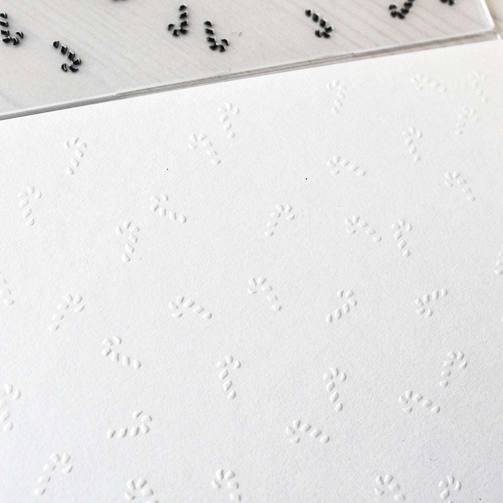 Geprägtes Zuckerstangenmuster auf weißem Papier mit einem Alexandra Renke Prägefolder, gekrönt von einem Alexandra Renke Klarsichtstempel mit schwarzem Zuckerstangen-Gewusel-Muster.