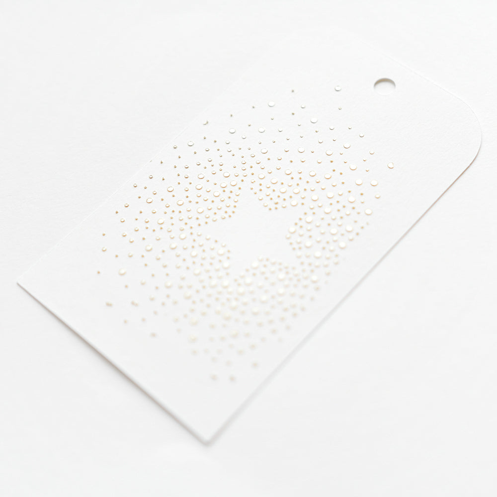 Weißer Geschenkanhänger mit einem zentralen Sternmuster aus kleinen goldenen Punkten, erstellt mit der "Schablone Stern aus Punkten" von Alexandra Renke.