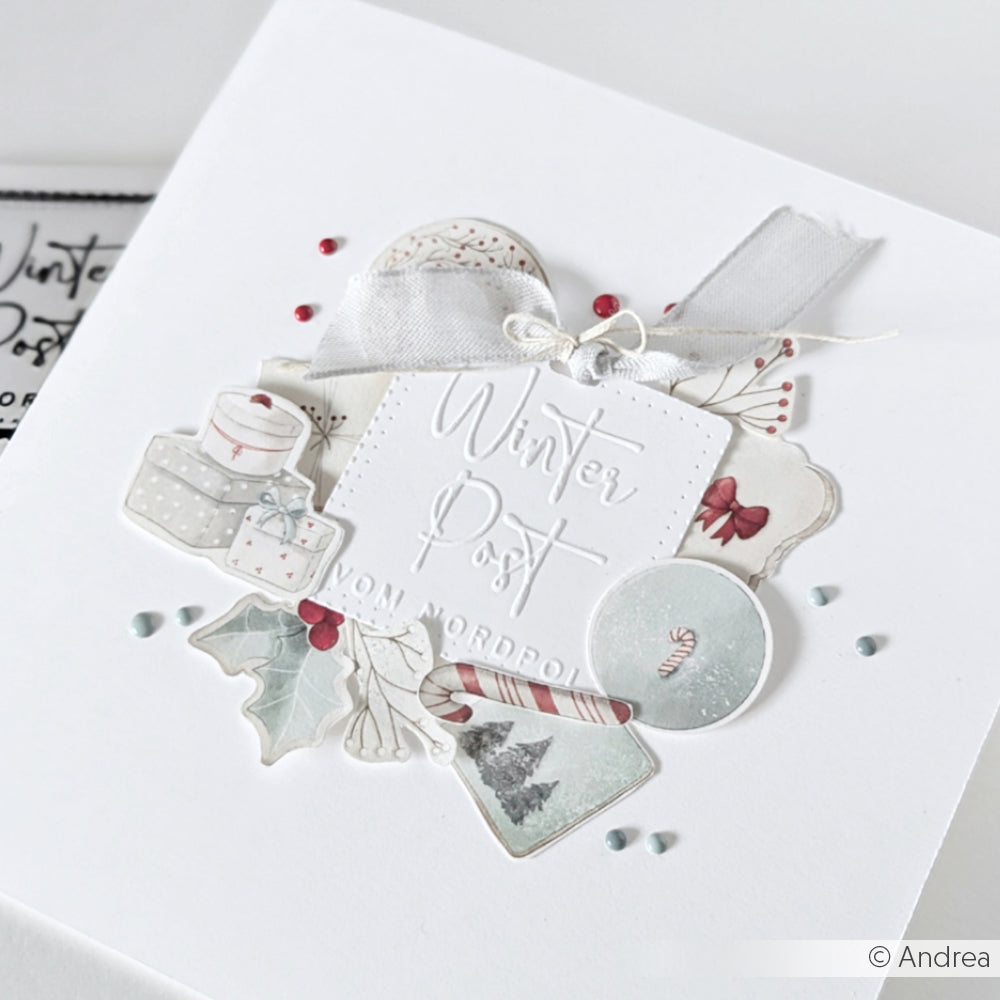 Eine weiße Weihnachtskarte von Alexandra Renke, verziert mit winterlichen Illustrationen, einem Band, dem Text "Winterpost" und eleganten Designpapier-Akzenten für einen charmanten saisonalen Look.