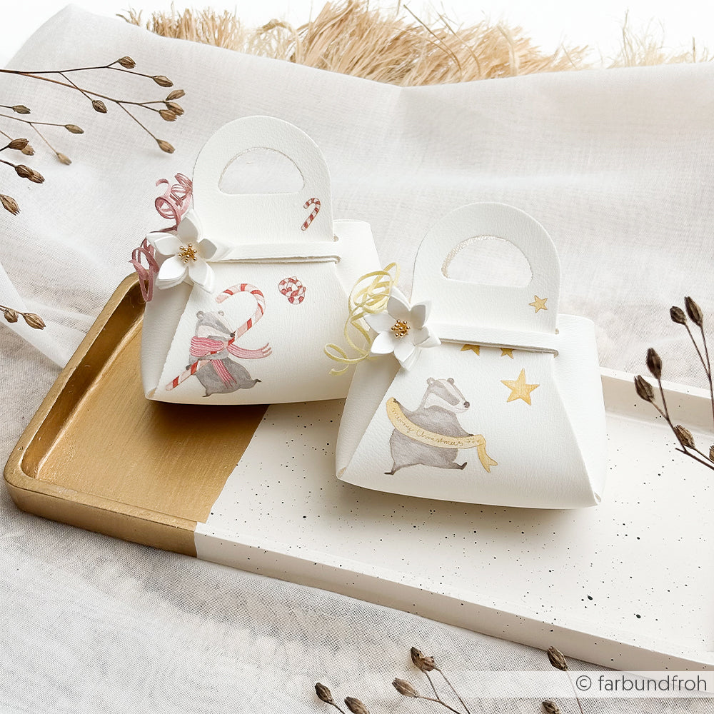 Zwei weiße Geschenktüten mit Dachs-Motiven und Weihnachtsmotiven für Bastelprojekte.