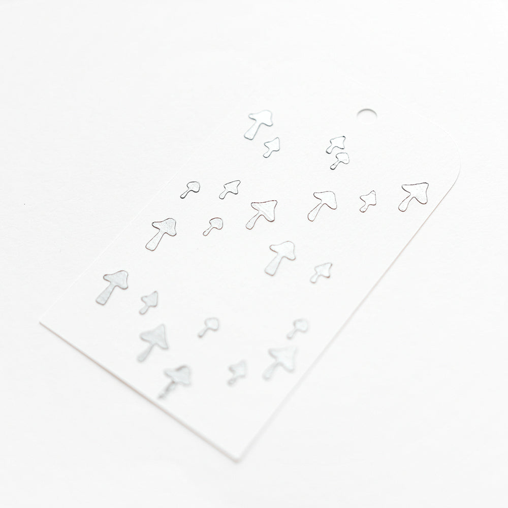 Weiße Karte mit den silbernen Pilzaufklebern von Alexandra Renke in verschiedenen Größen, übersichtlich angeordnet - ideal für Schablonen-Papierprojekte oder zur Aufwertung Ihrer liebsten Stencil-Pilzlandschaft-Motive.