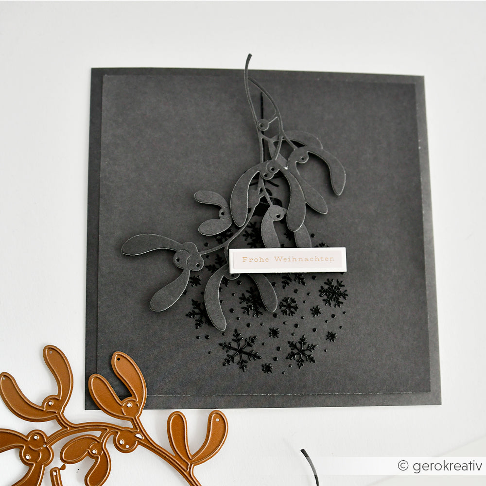 Handgefertigte Karte mit einem grauen Mistelzweig-Stanzteil, einer Weihnachtskugel-Schablone und dem Schriftzug Frohe Weihnachten.