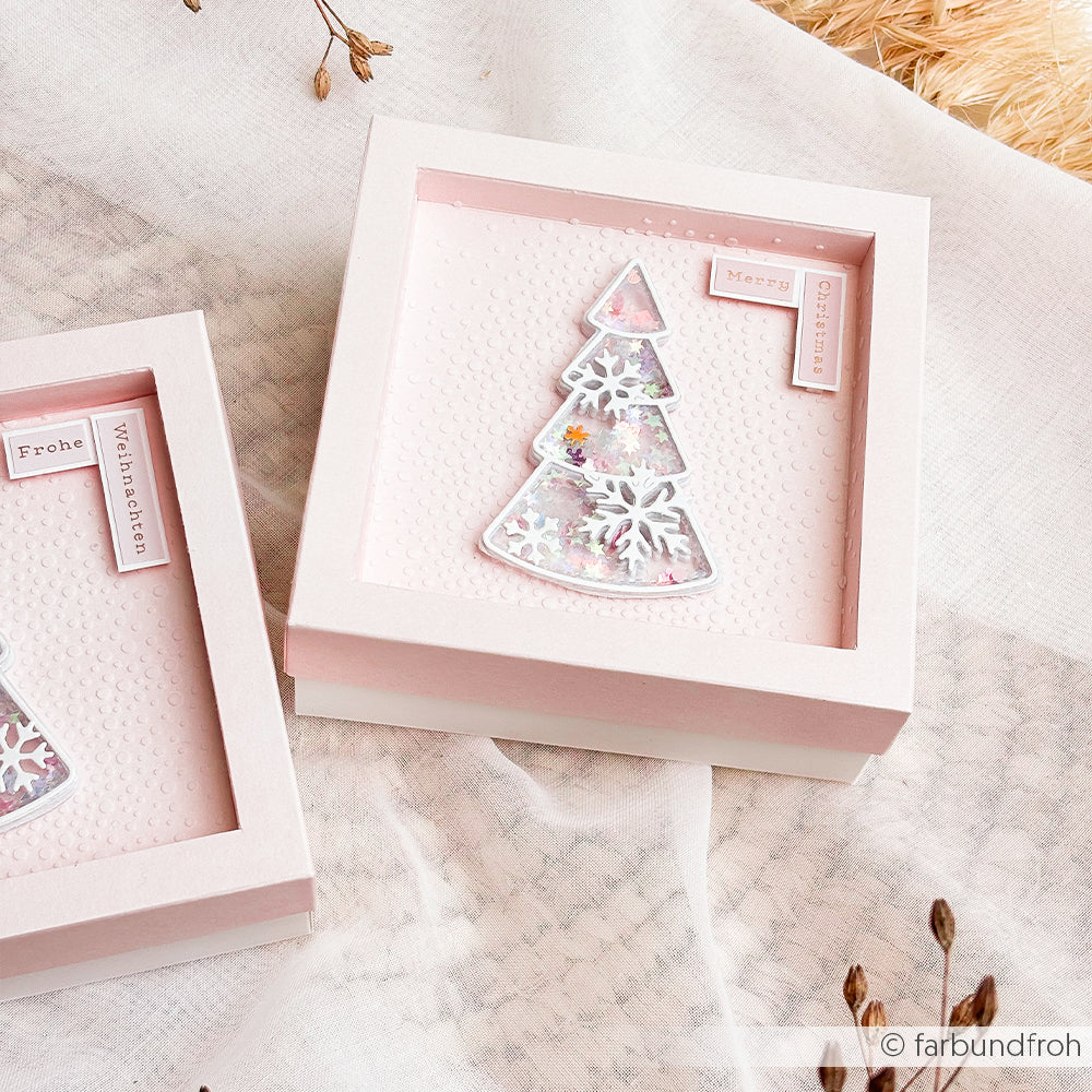 Zwei quadratische, rosa Geschenkboxen, jeweils mit einem wiederverwendbaren Schablonen-Weihnachtsbaum als Schüttel-Dekor.