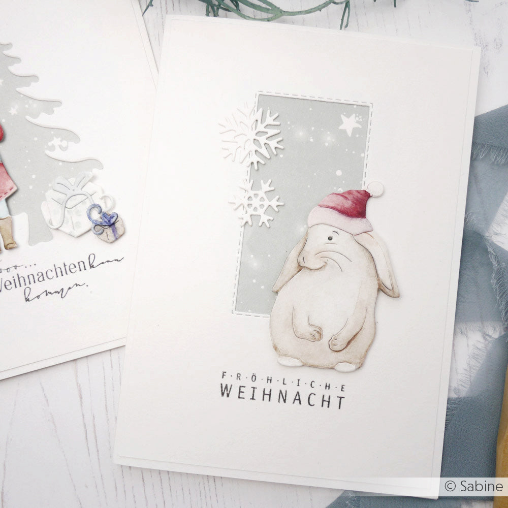 Handgemachte Weihnachtskarte von Alexandra Renke mit einem Hasen mit Weihnachtsmannmütze, Schneeflocken und "Fröhliche Weihnacht". Die Karte ist mit einem Klarsichtstempel versehen, der für klare Details sorgt - ideal, um festliche Familienzeitstimmung zu verbreiten!.