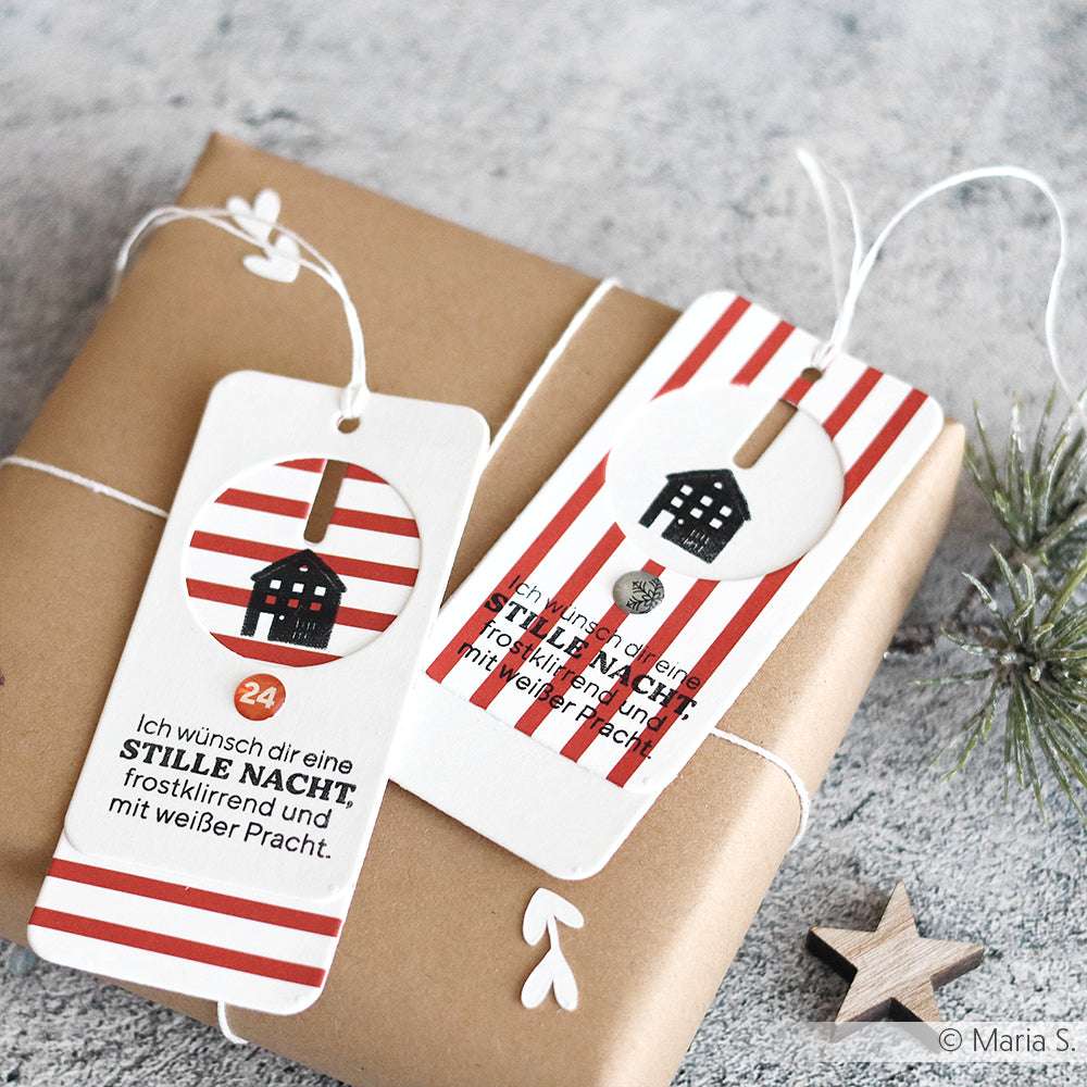 Geschenkverpackung aus braunem Papier mit zwei gestreiften Anhängern mit deutschem Text aus dem Alexandra Renke Clear Stamp Weihnachtsset und kleinen Hausillustrationen, die neben dem Tannendekor platziert sind.