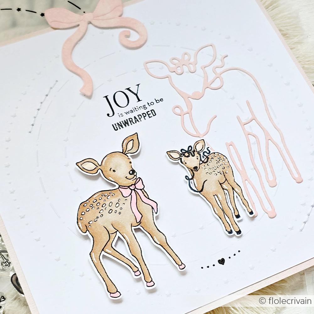Handgefertigte Karte von Alexandra Renke mit zwei illustrierten Rehkitzen, einer rosa Schleife und dem Text "Joy is waiting to be unwrapped" (Freude wartet darauf, ausgepackt zu werden), mit subtilen Winterruhe-Vibes und Photopolymer-Klarsichtstempel-Details.