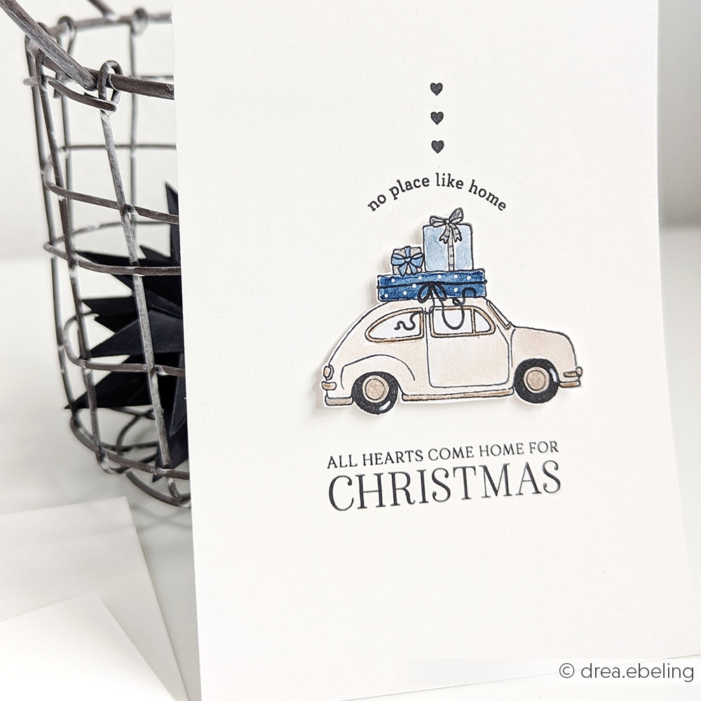 Grußkarte von Alexandra Renke mit einem Auto mit Geschenken, Herzen darüber und dem Text "All hearts come home for Christmas". Hergestellt mit Photopolymer-Klarsichtstempel für gestochen scharfe, charmante Weihnachtsdetails.