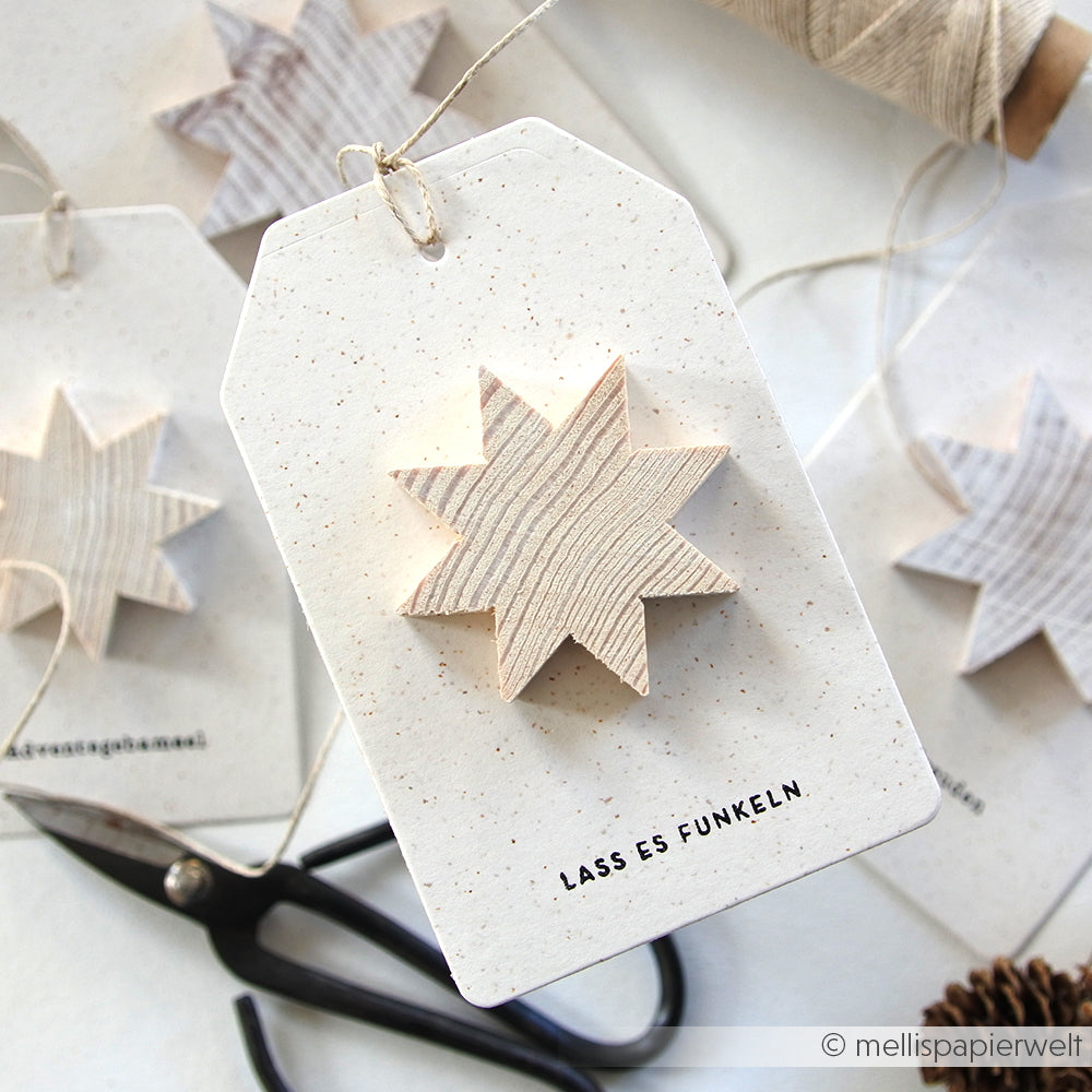 Anhänger mit einem Stern aus Holz, dem Text LASS ES FUNKELN, einer Schere, einer Schnur und einem Alexandra Renke Clear Stamp Design im Hintergrund.