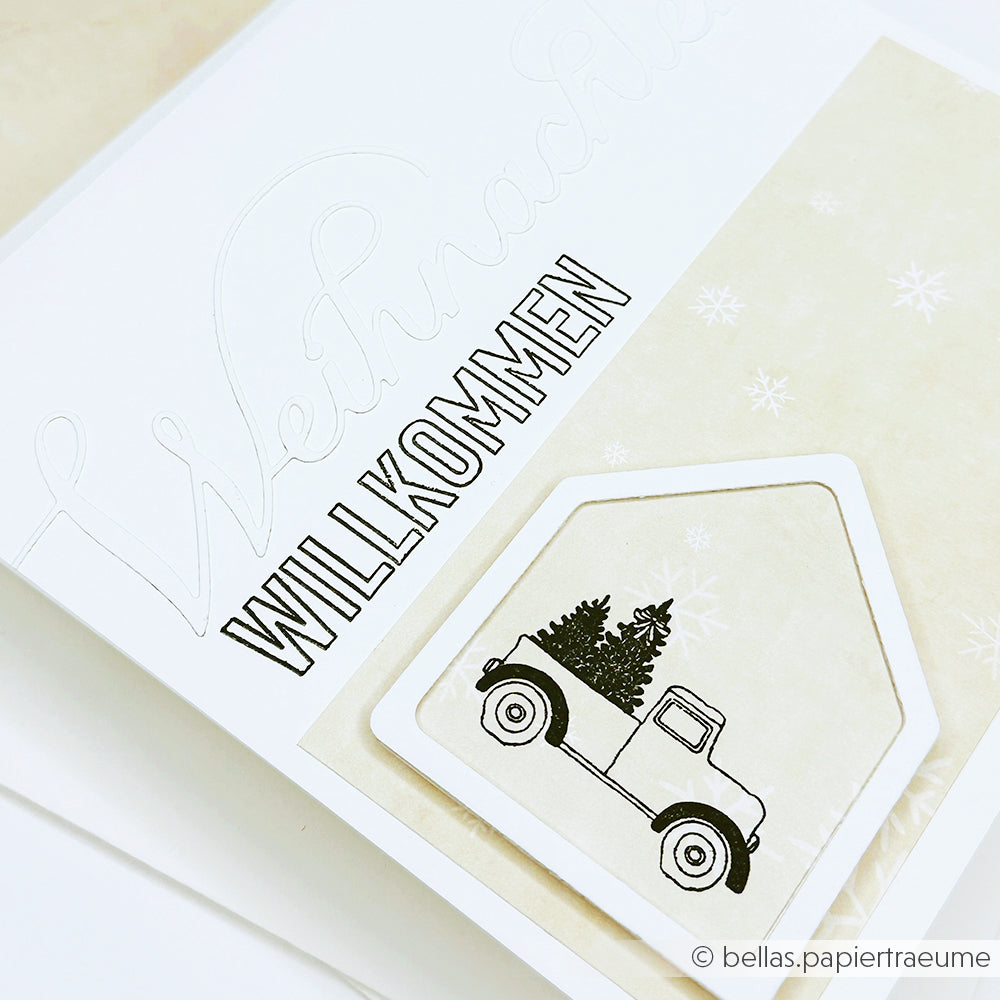 Weiße Karte mit dem Text WILLKOMMEN, einem Lastwagen, der Bäume transportiert, und einem schwachen Weihnachtsmotiv im Hintergrund - perfekt für Papierprojekte mit Alexandra Renke Photopolymer Stempel oder Clear Stamp Designs.