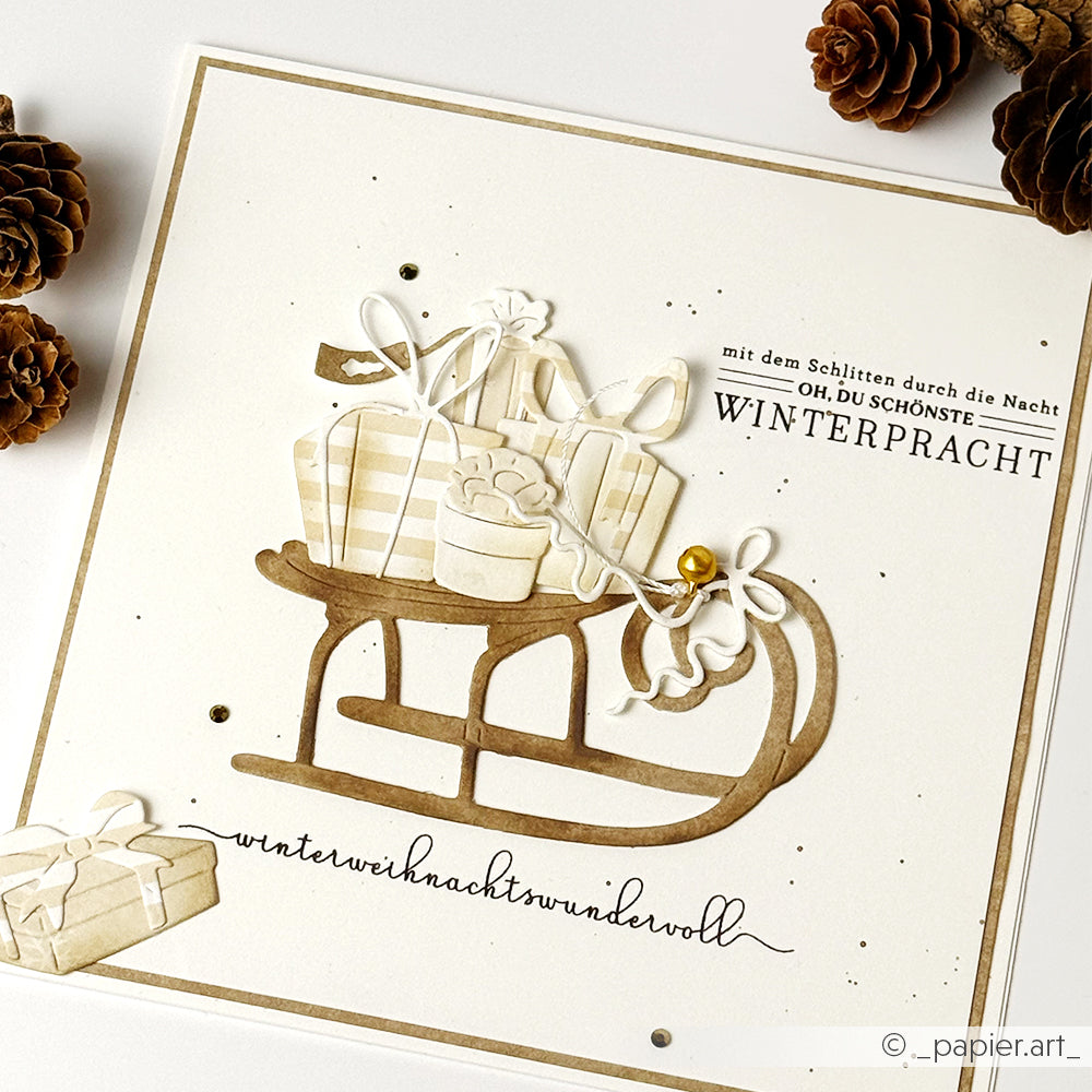 Handgemachte Karte von Alexandra Renke mit einem Schlitten mit Geschenken, Tannenzapfen und deutschen Weihnachtsgrüßen. Die Karte wurde mit einem Clear Stamp für gestochen scharfe Details entworfen und ist perfekt, um die Weihnachtszeit auf einem weißen Hintergrund zu feiern.