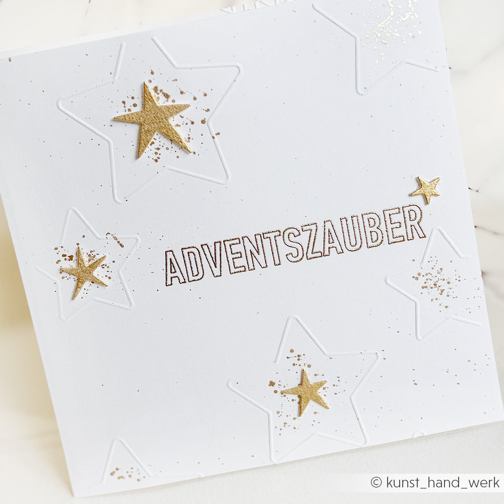 Weiße Karte mit geprägten Sternen, goldenen Sternakzenten und "ADVENTSZAUBER" in umrissenen Buchstaben in der Mitte, hergestellt mit Alexandra Renke Photopolymer-Klarsichtstempel für gestochen scharfe, präzise Details.