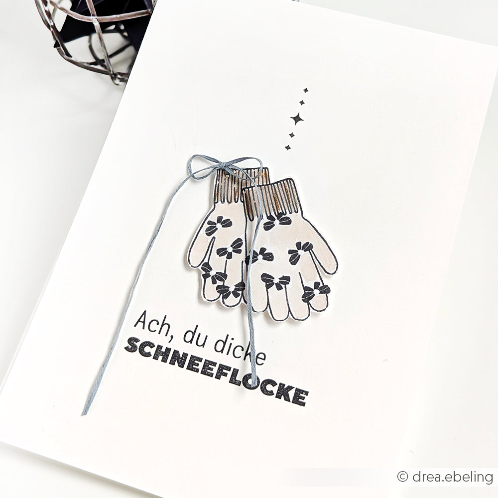 Diese Karte von Alexandra Renke zeigt illustrierte Fäustlinge, die mit einer Schnur zusammengebunden sind, und den deutschen Text "Ach, du dicke SCHNEEFLOCKE", der sich perfekt mit Ihren Lieblingsmotiven von Eiskristallträume Clear Stamp oder Photopolymer kombinieren lässt.