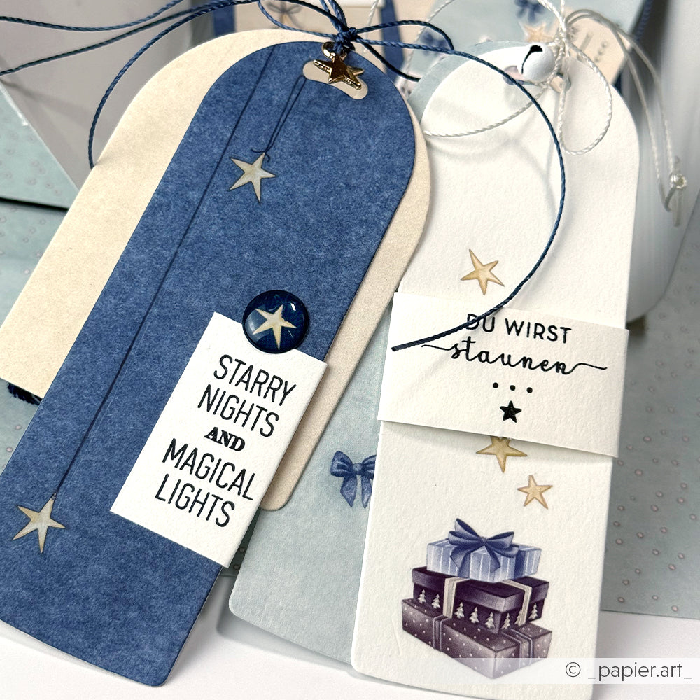 Zwei dekorative Alexandra Renke Geschenkanhänger mit Sternen - einer mit der Aufschrift STARRY NIGHTS AND MAGICAL LIGHTS", der andere mit Geschenken - eignen sich perfekt für die Kombination mit Ihrem Lieblings-Stempel aus Klarsichtfolie oder Photopolymer für eine persönliche Note.