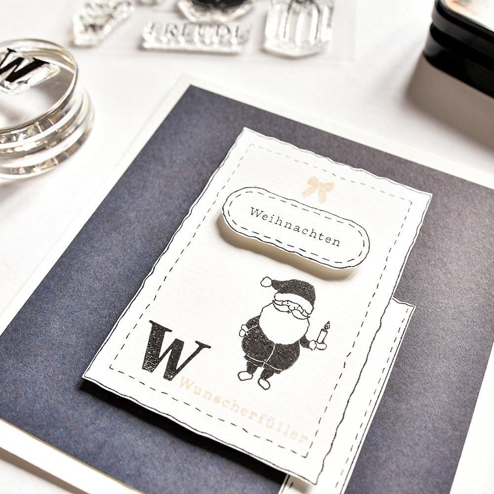 Handgemachte Weihnachtskarte von Alexandra Renke mit einer schwarz-weißen Weihnachtsmann-Illustration und deutschem Text, hergestellt mit Photopolymer-Klarsichtstempeln auf dunklem Hintergrund - perfekt, um Weihnachtsfreude zu verbreiten.