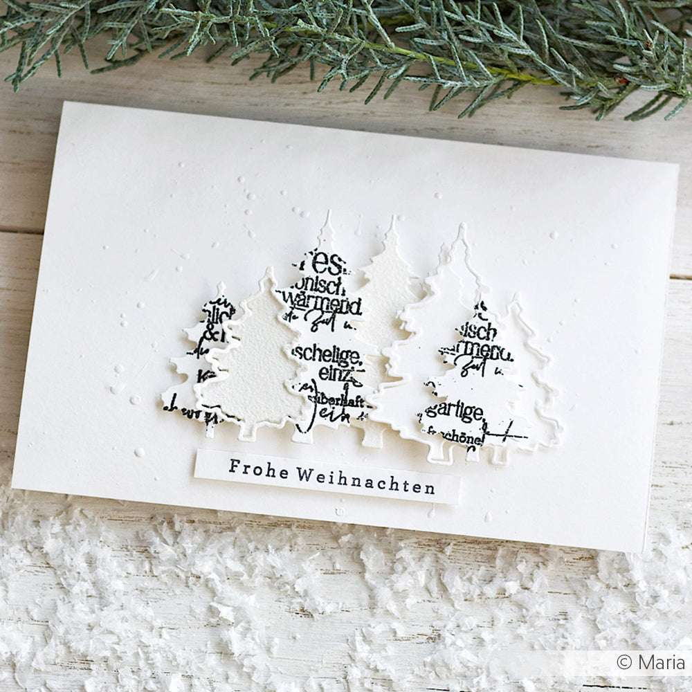 Weiße Weihnachtskarte mit drei Papierbäumen aus der Alexandra Renke Motivstanze Tannen-Duo auf einer verschneiten Fläche mit dem Motiv "Frohe Weihnachten" - ideal für festliche Dies für Papierbasteln.
