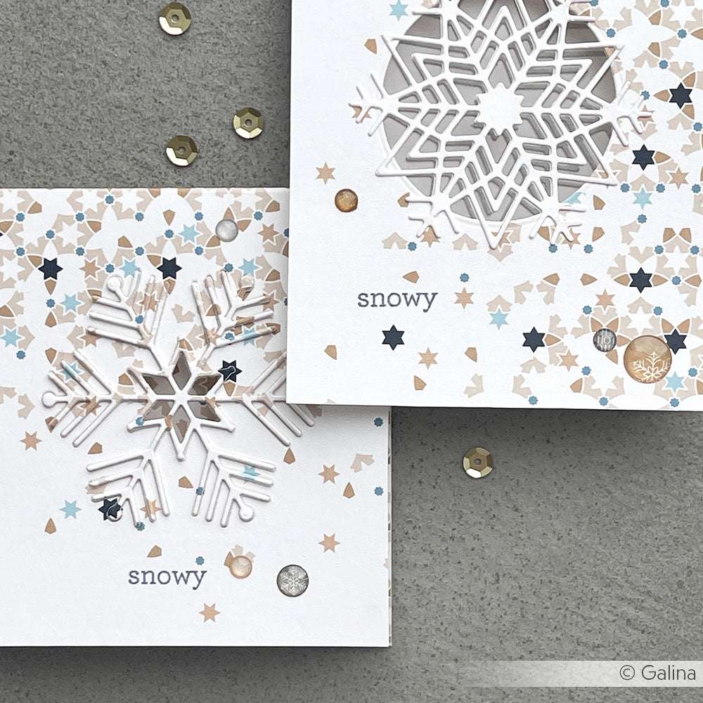 Zwei weiße Weihnachtskarten mit kunstvollen Schneeflocken, die mit den Alexandra Renke Eiskristallstempeln ausgestanzt wurden, zarten Sternenmustern und dem Wort "snowy" auf jeder Karte.