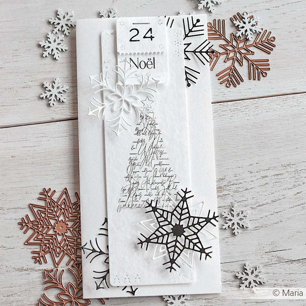 Weiße Weihnachtskarte mit Schneeflocken-Dekorationen und Schrifttext, umgeben von metallischen Schneeflockenausschnitten, die mit den Alexandra Renke Eiskristall Stanzformen hergestellt wurden und für einen festlichen Touch sorgen.