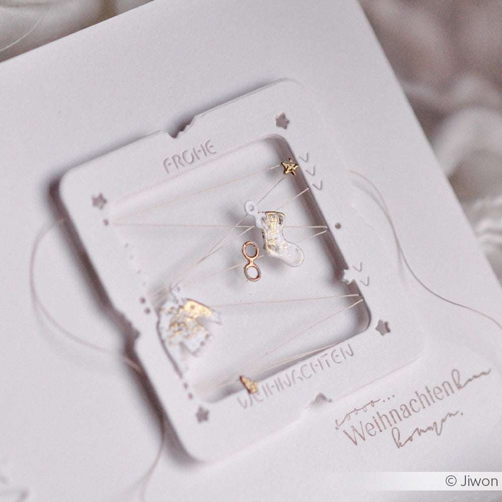 Zarter goldener und weißer Weihnachtsschmuck auf einer festlichen weißen Karte mit ausgestanzten Sternen, hergestellt mit der Mini-Wintergarderobe von Alexandra Renke für zusätzlichen Charme.