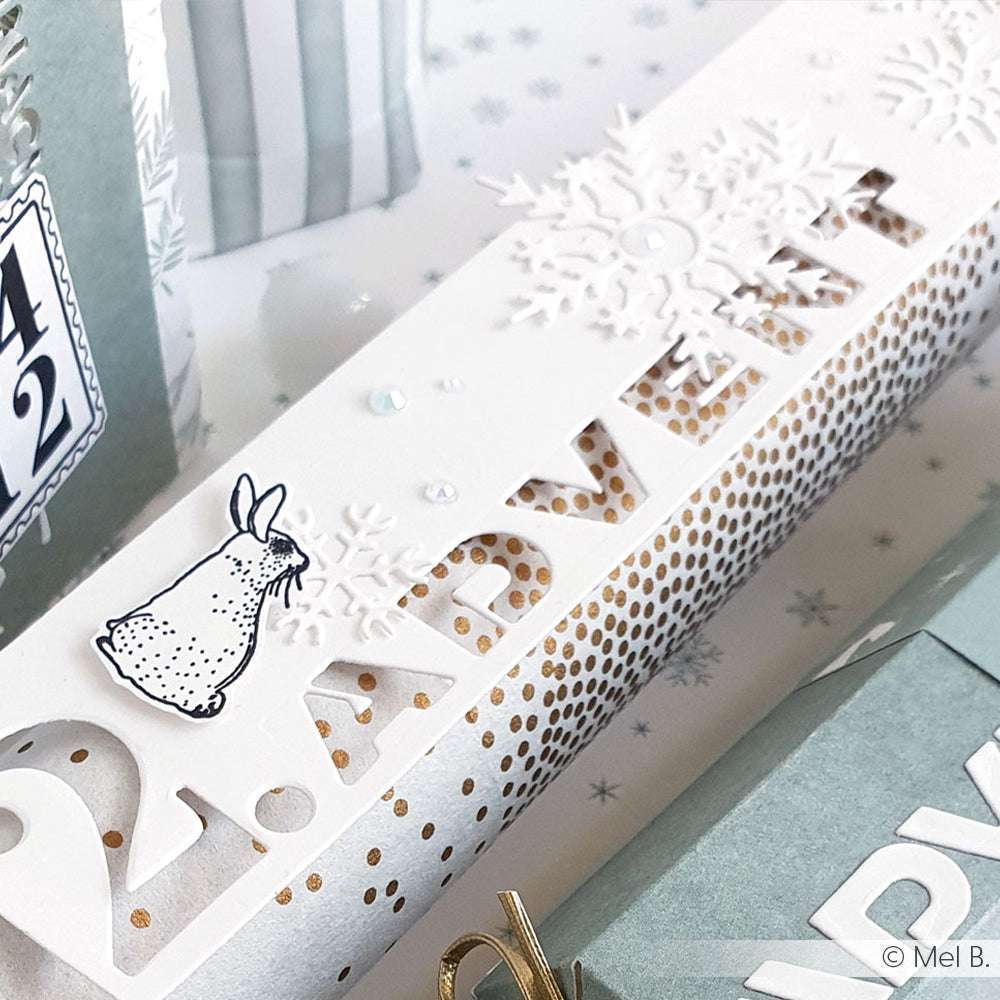 Weiße Adventskalenderschachtel von Alexandra Renke mit goldenen Punkten, Akzenten aus Designpapier und Schneeflocken, die mit der Stanze Motivstanze Schneeflocke ausgestanzt wurden. Abgerundet mit einem kleinen illustrierten Hasen.