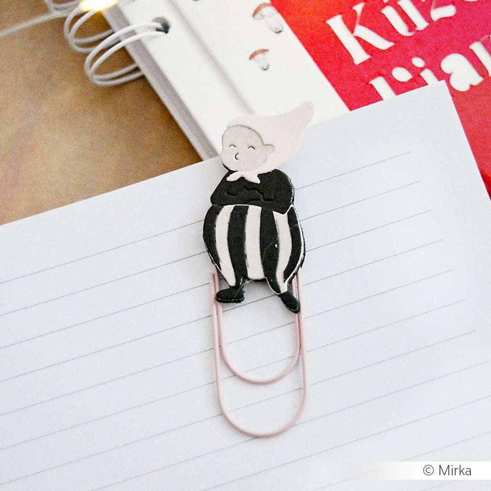 Eine Büroklammer mit einem Cartoon-Topper, wie zum Beispiel die skurrile Motivstanze Wichtel Sven von Alexandra Renke, sichert liniertes Papier neben einem Spiralhefter.