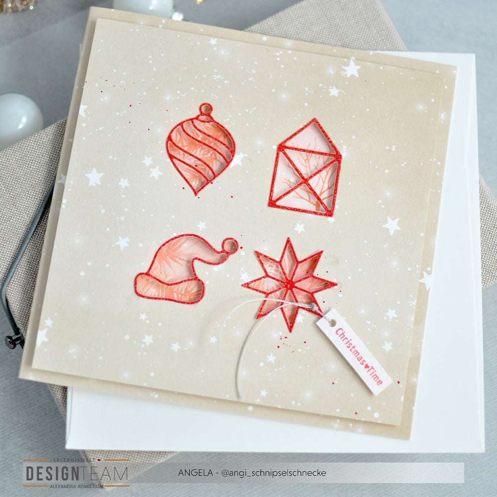 Diese quadratische Weihnachtskarte von Alexandra Renke zeigt rote String-Art-Ornamente, Sterne und einen festlichen Anhänger auf einem verschneiten Hintergrund, der mit aufwendigen Motivstanze-Details veredelt wurde, die für zusätzlichen Weihnachtszauber sorgen.