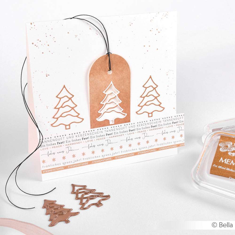 Weiße Weihnachtskarte mit kupferfarbenen Weihnachtsbaumausschnitten, die mit der Alexandra Renke Motivstanze Tanne, einem passenden Geschenkanhänger und einem Stempelkissen auf einer weißen Fläche hergestellt wurden.