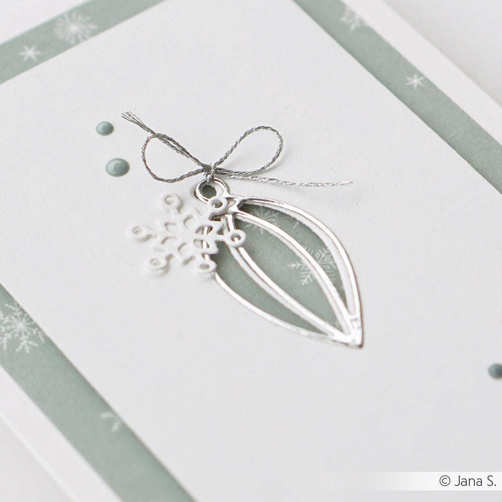 Minimalistische Weihnachtskarte von Alexandra Renke mit silbernem Ornament, Schneeflocke und Schleife auf hellgrünem und weißem Hintergrund - gestaltet mit der Motivstanze Baumkugel für eine einzigartige Note.