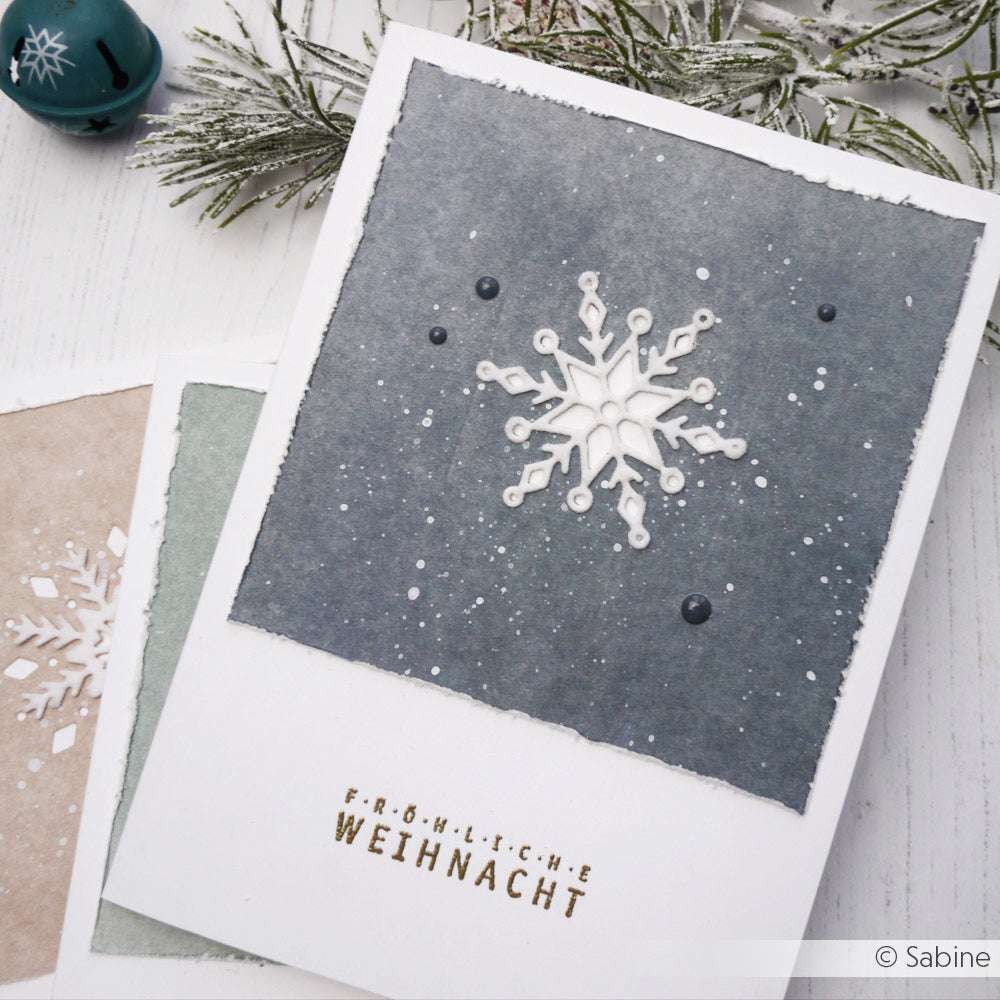 Handgemachte Weihnachtskarte von Alexandra Renke mit einer weißen Schneeflocke (Motivstanze Schneeflocken) auf dunklem Hintergrund und "Fröhliche Weihnacht" in goldenen Buchstaben.