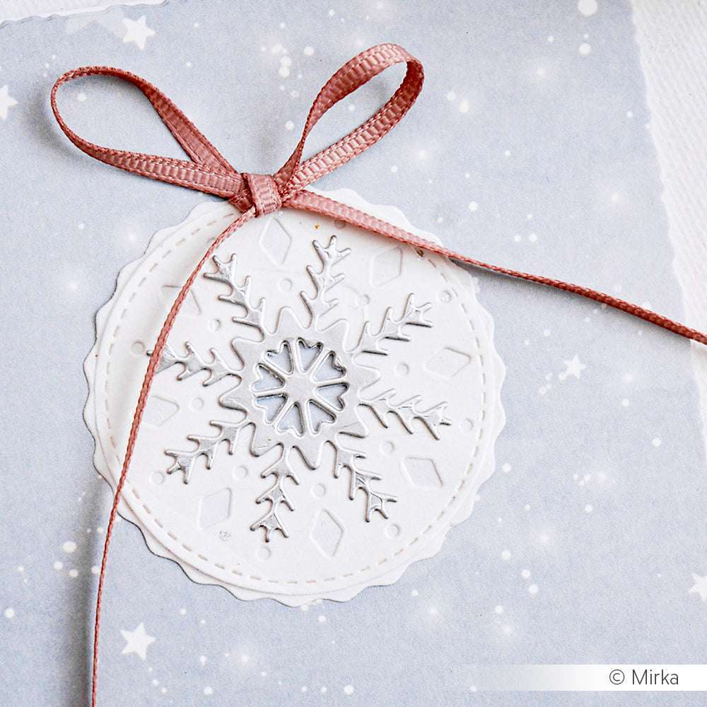 Alexandra Renke weißes Schneeflocken-Ornament mit rosa Schleife, detailliertes Schneeflocken-Muster, dargestellt auf einem hellen, verschneiten Hintergrund.