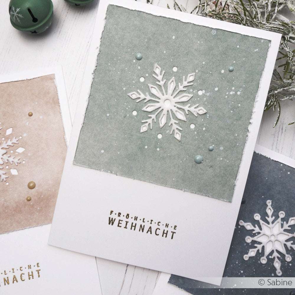 Eine handgefertigte Weihnachtskarte von Alexandra Renke zeigt ein Negativ-Schneeflocken-Muster auf grünem Hintergrund, akzentuiert mit "Fröhliche Weihnacht".