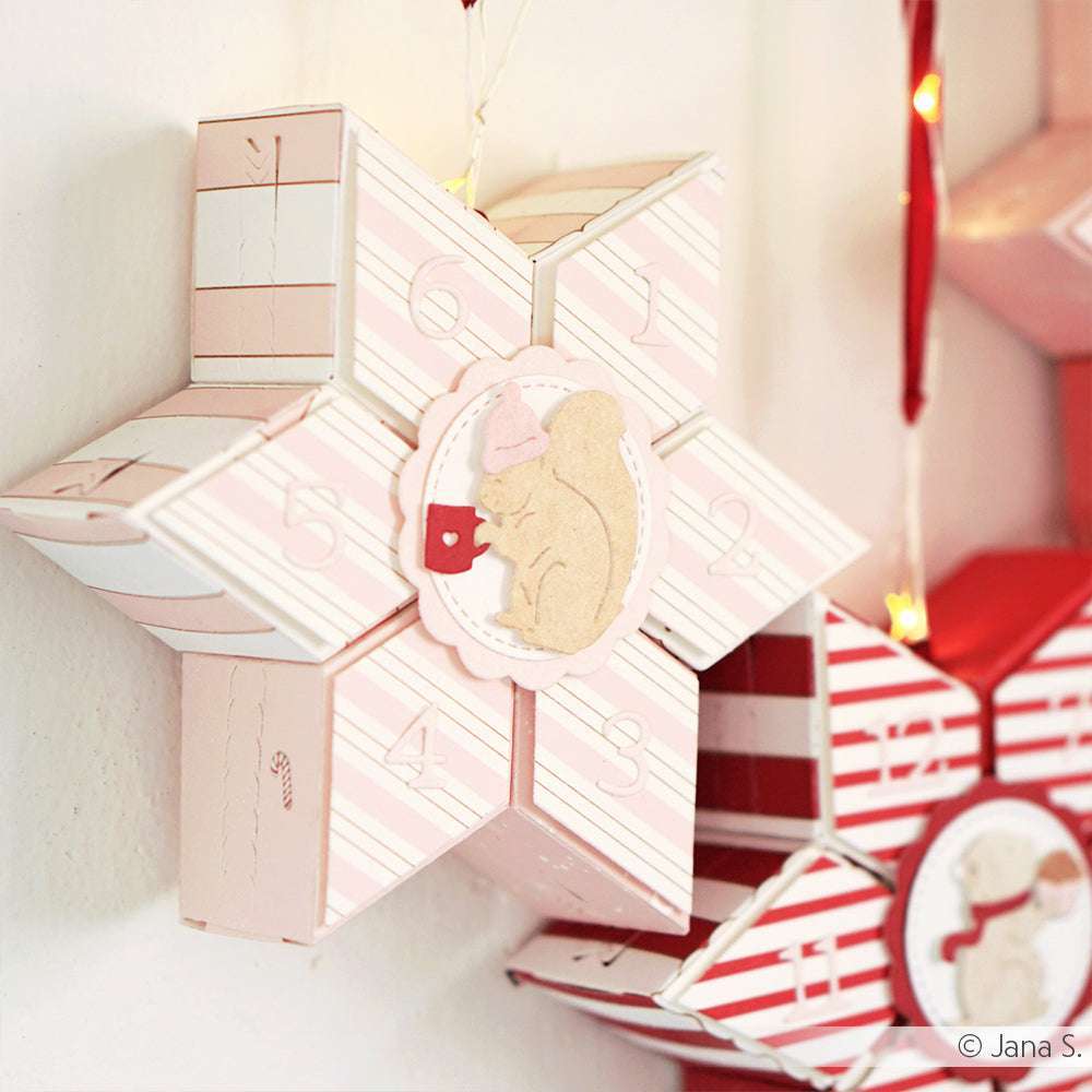 Rosa-weiße sternförmige Schachtel von Alexandra Renke mit einem Eichhörnchenmotiv, nummerierten Feldern und festlichen Lichtern im Hintergrund - perfekt für die Feiertage und inspiriert von Tee trinkende Tierchen und Motivstanze Tier Duo Stanzsysteme.