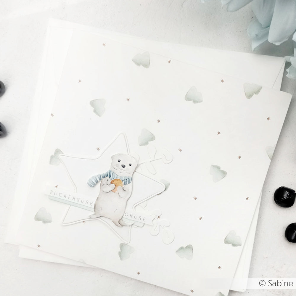 Ein niedlicher Eisbär mit Schal, entworfen von Alexandra Renke mit Stanzsystemen, befindet sich auf einer weißen Karte, die mit Sternen- und Baummustern verziert ist.