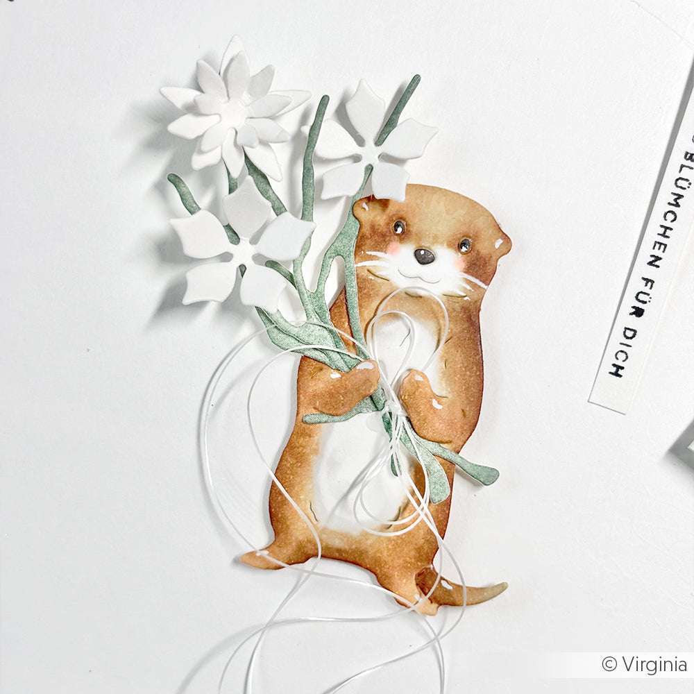 Ein charmanter Otter aus Alexandra Renkes Mäuserich & Otter Motivstanze Tier Duo hält weiße Blumen mit grünen Stängeln vor einem sauberen weißen Hintergrund.