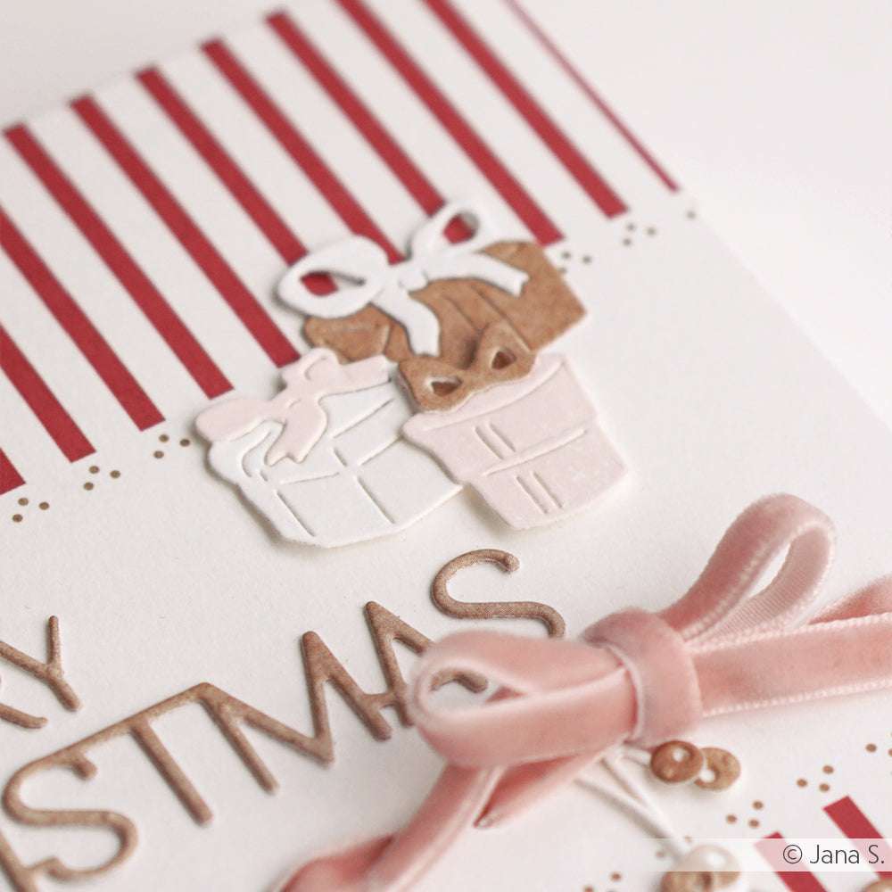 Nahaufnahme einer handgefertigten Weihnachtskarte von Alexandra Renke, hergestellt mit Designpapier und dem Motivstanze Geschenke Quintett. Mit Geschenkillustrationen und einer rosa Samtschleife auf gestreiftem Hintergrund.