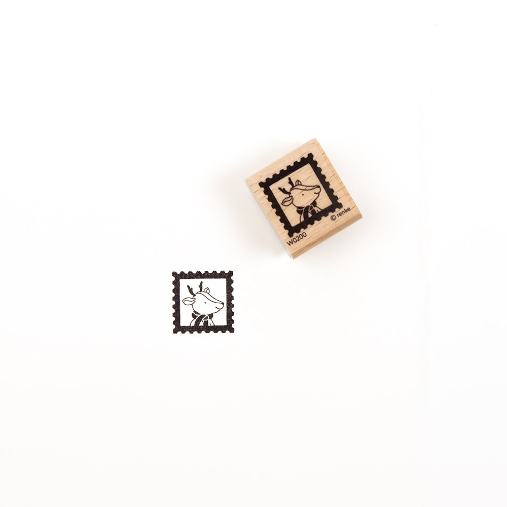 Ein Holzstempel mit der Abbildung eines Rentiers in einem Briefmarkenrahmen sowie ein Stempelabdruck desselben Holzstempel-Motivs.