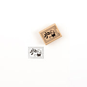 Ein Holzstempel und sein Abdruck, der eine Maus zeigt, die einen Mistelzweig in einem Briefmarkenrahmen hält.