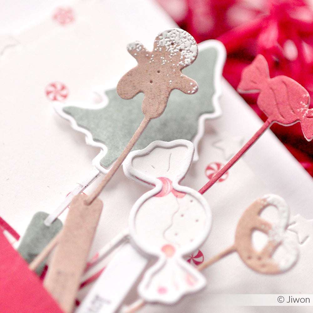 Festliche Lebkuchen, Süßigkeiten und Weihnachtsbäume, die mit Alexandra Renke DieCut Systemen und farbenfrohen Designpapieren ausgestanzt wurden, sind wunderschön auf einer weißen Fläche arrangiert.