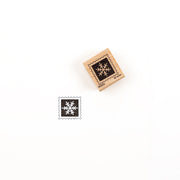 Ein quadratischer Holzstempel mit einem Schneeflockenmotiv und dem dazugehörigen Abdruck in schwarzer Tinte, der den Holzstempel zeigt.