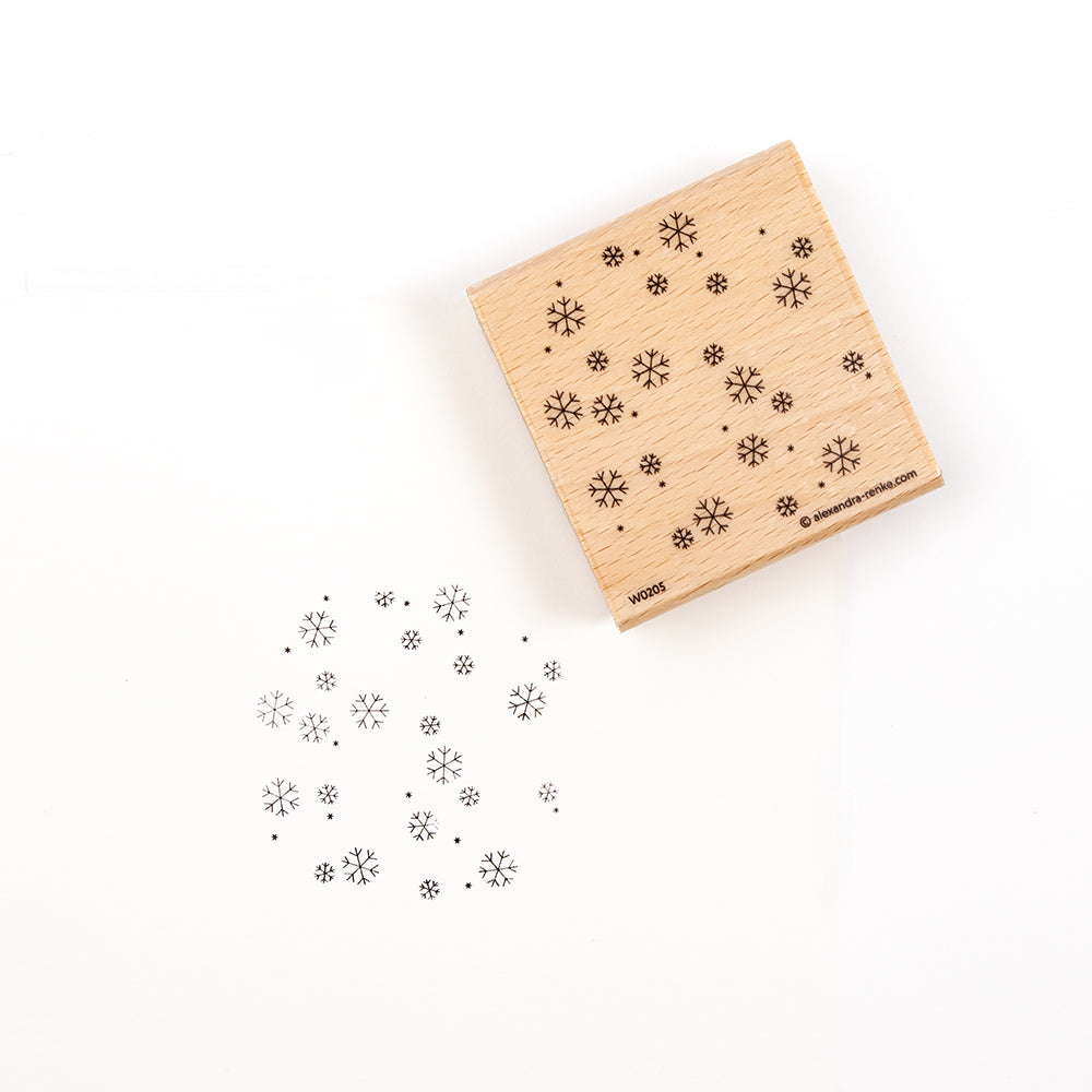 Ein Holzstempel mit einem Schneeflockenmuster und seinem Abdruck auf weißem Hintergrund, der die Vielseitigkeit des Holzstempels verdeutlicht.