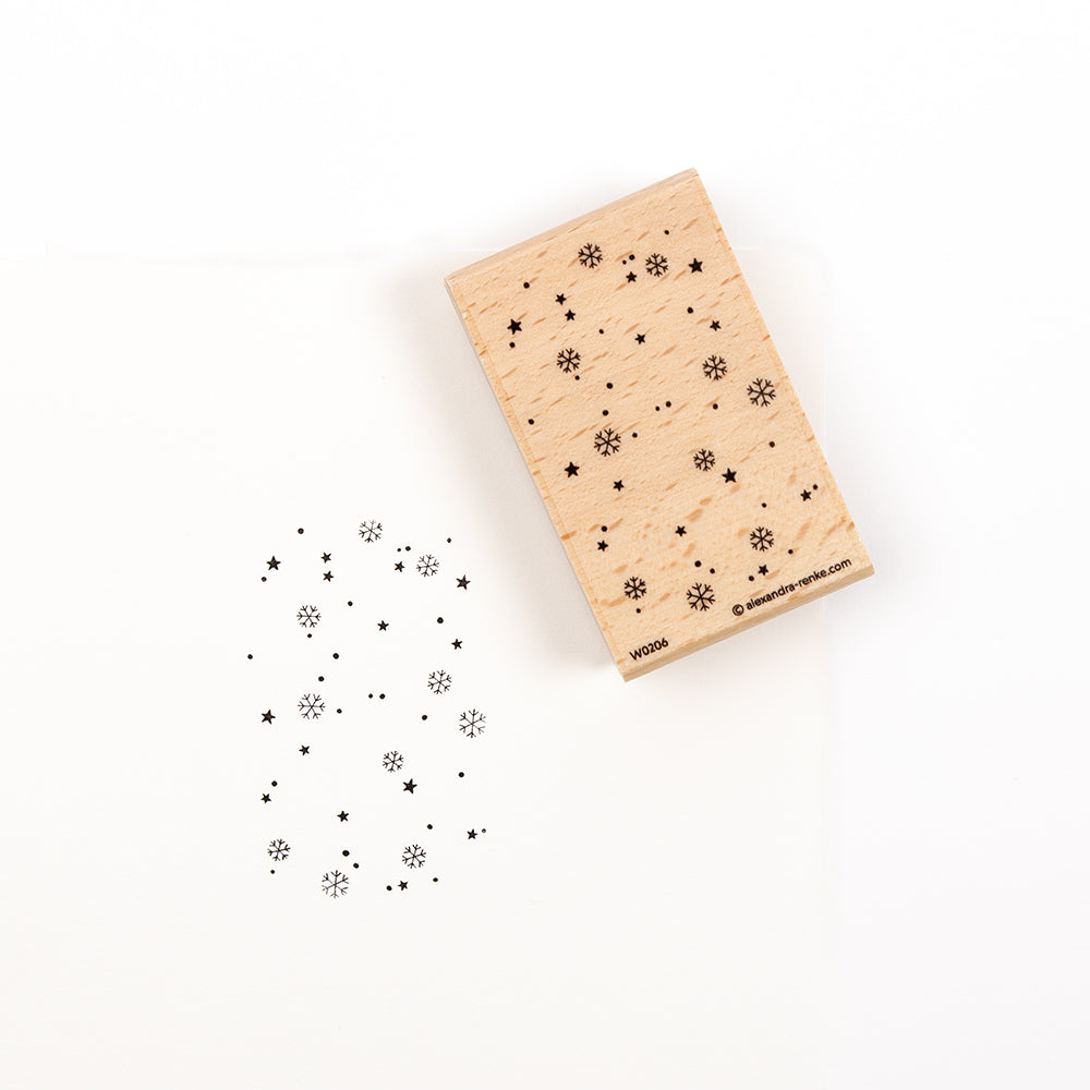 Ein Holzstempel mit einem „Schneeflocken & Sterne“-Motiv neben dem Stempelabdruck.